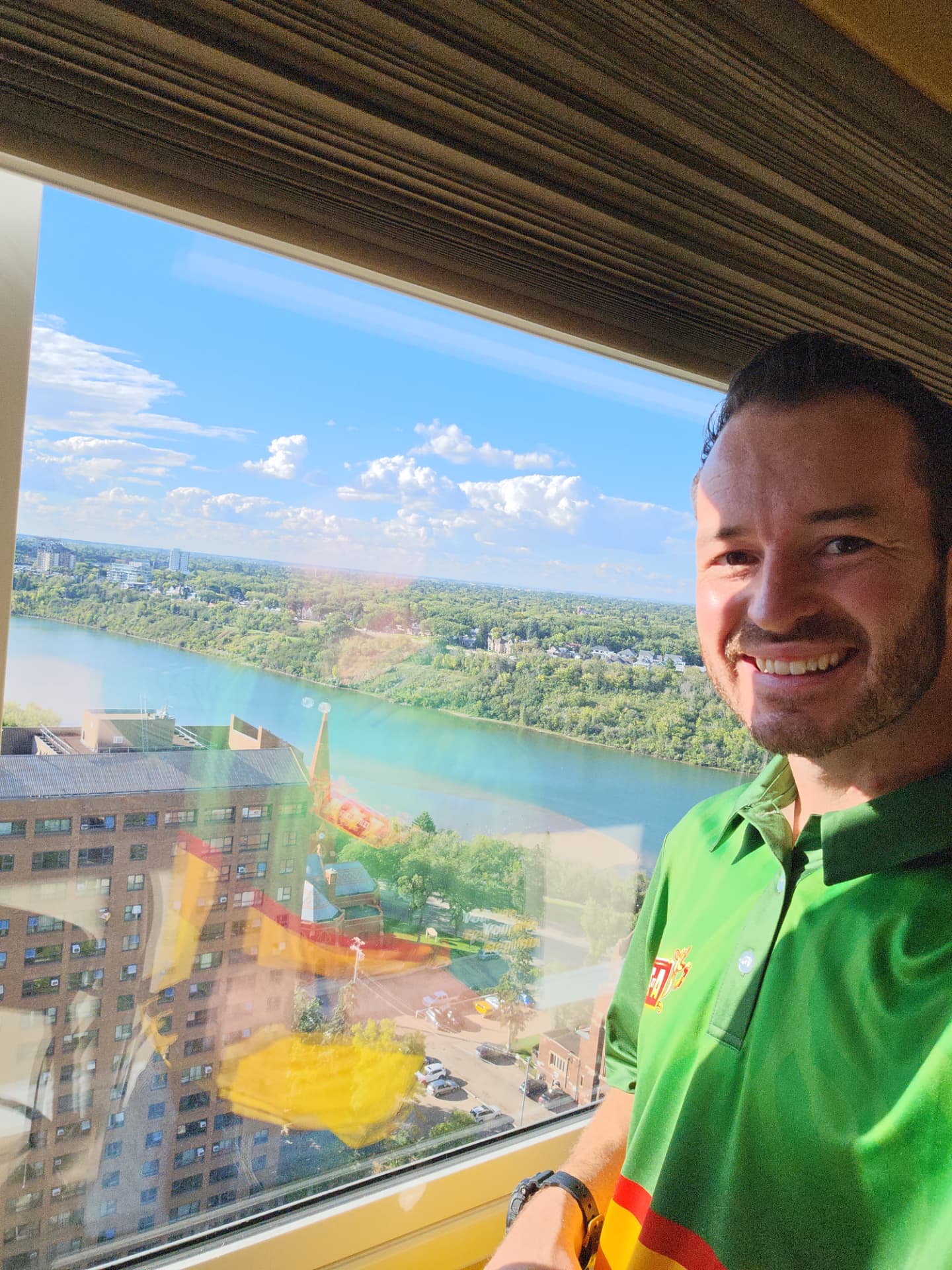 Adam, owner of A to Z, smiling in his branded shirt with the Saskatoon river valley behind him